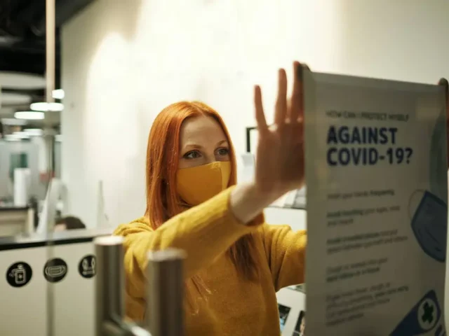 Female business owner wearing mask installing COVID-19 signage during the pandemic.